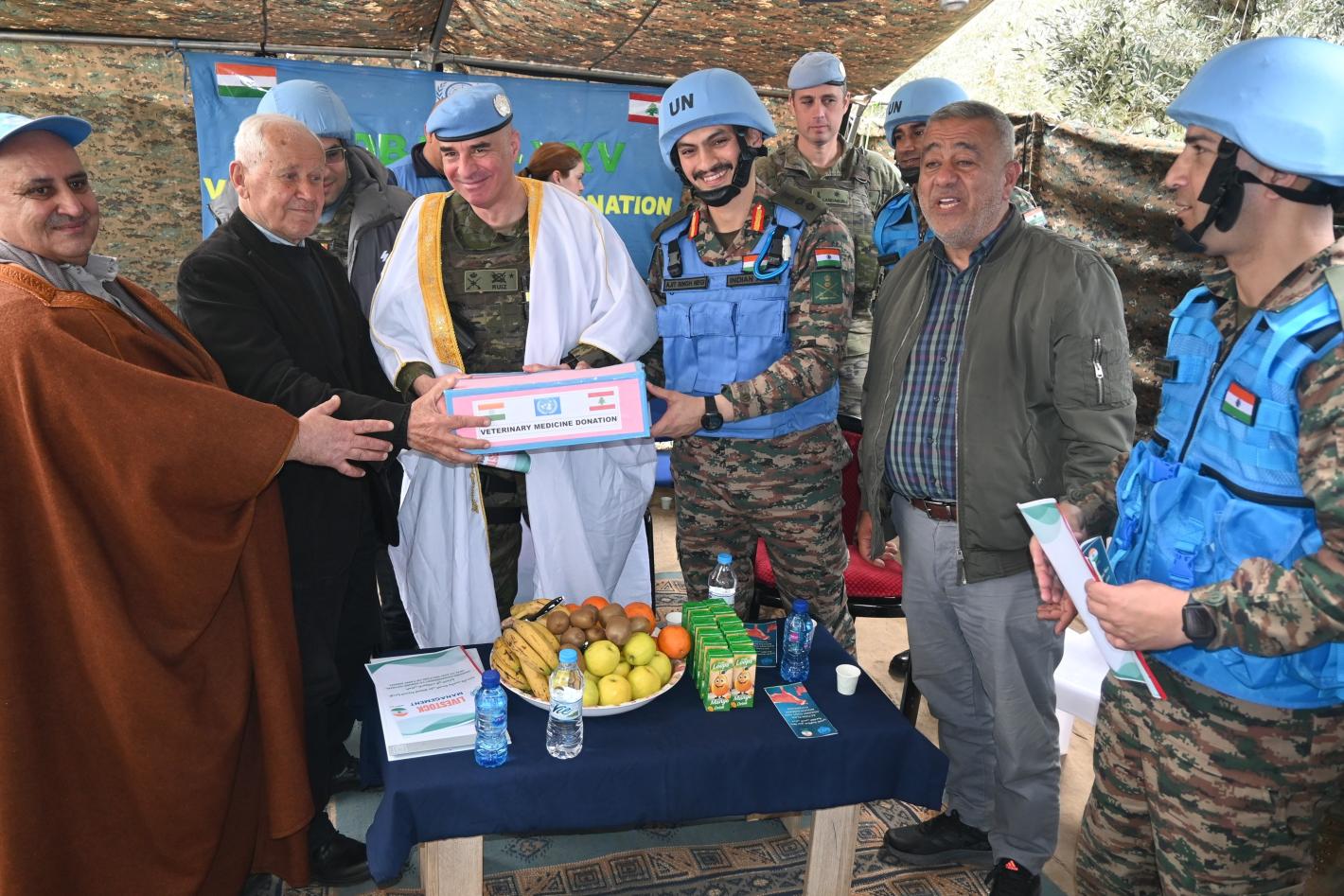 A group of peacekeepers and civilians standing around a table where food is served.