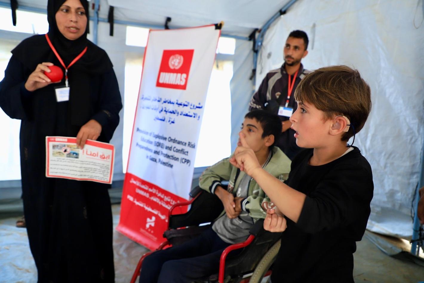 A woman is holding a red ball and a poster with two kids and a man beside her