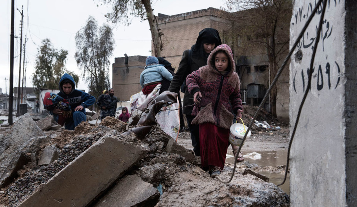 A family displaced by fighting between ISIS and Iraqi security forces carry their belongings as they walk through the destroyed western neighbourhood of Al Mamum, near Mosul, Iraq. Photo: UNICEF/Alessio Romenzi